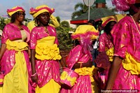 Women wearing bright pink and yellow outfits at the Avondvierdaagse parade in Paramaribo, Suriname.