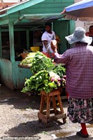 Versión más grande de Una mujer rocía agua sobre sus greens en Stabroek Mercado en Georgetown, Guyana.