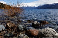 Larger version of Traful Lake with rocks in the foreground and distant snow-capped mountains, north of Bariloche.