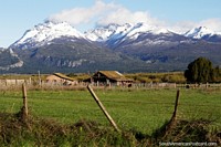 Cortijo, granero y tierra de pastoreo con gigantescas montañas cubiertas de nieve alrededor de Trevelin. Argentina, Sudamerica.