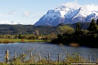 Laguna acuosa, tierras de cultivo y montañas nevadas, un caballo pasta, la Ruta 259 hasta la frontera desde Trevelin. Argentina, Sudamerica.