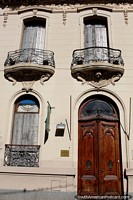 Iron balconies feature on this facade with a tall wooden door in Santa Fe. Argentina, South America.
