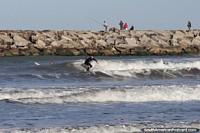 Surfando as ondas na praia de Mar del Plata com os pescadores atrás. Argentina, América do Sul.