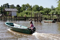 Man in a motorboat travels along the river past a wooden jetty in Tigre, Buenos Aires. Argentina, South America.