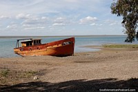 Orange wooden fishing boat sits on the beach at high tide in San Antonio Oeste.