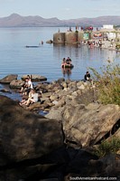 Versión más grande de Rocas donde la gente disfruta del sol en la playa junto al lago en Bariloche.