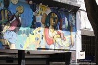 Mulher sentada com bebida, mural colorido, vitrine em Rosário.