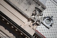 Una figura sentada junto a un pilar, una ventana y un techo escamoso, la fachada del Palacio de Gobierno de Jujuy.