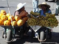 Melons and bananas in wheelbarrows being sold by 2 ladies in Cochabamba.
