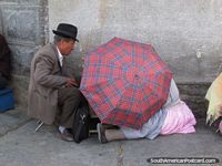 Man and woman conduct business behind an umbrella on the pavement in Oruro. Bolivia, South America.