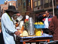 Juice stand in Desaguadero, a woman cuts pineapple and a man drinks. Bolivia, South America.