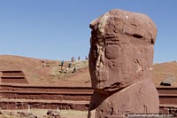 A crumbly stone head, people excavating on the hill behind, Tiwanaku Ruins.