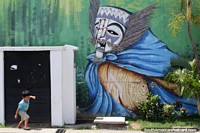 Larger version of Masked face with feathers and a blue cape, mural in Santa Cruz.