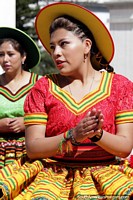 Woman in a red top, yellow dress and hat dancing in the plaza in Potosi.