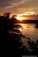 Increíble puesta de sol naranja sobre el río en Riberalta como un barco de río pasa. Bolivia, Sudamerica.