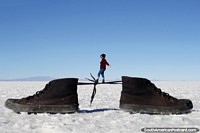 Larger version of Woman walks across the tied laces of a pair of shoes, a great photo showing perspective tricks in photography at the Uyuni salt flats.