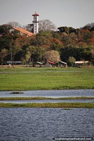 Looking across the water towards colorful trees and the church tower in San Ignacio de Velasco.