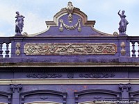 Larger version of 2 figures at the top of a purple historical facade in Rio Grande.