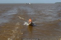 Um rapaz de Amazônia em uma canoa motorizada persegue o barco, Belém a Macapa. Brasil, América do Sul.
