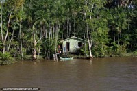 Um homem vaza a água do lado de fora da sua casa de Amazônia, canoa na frente, ao oeste de Belém. Brasil, América do Sul.