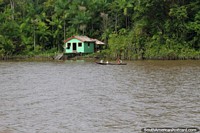 Familia en una canoa en el río fuera de su pequeña casa verde del Amazonas, al sur de Macapá. Brasil, Sudamerica.