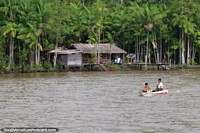 2 boys in a canoe with their house in the Amazon behind them, south of Macapa. Brazil, South America.