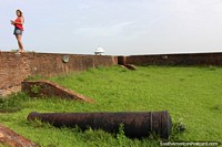 Menina em vermelho em uma parede de tijolos e um canhão no forte em Macapa. Brasil, América do Sul.