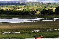 Homem em uma canoa de rio, pastos distantes e colinas em volta de Penedo. Brasil, América do Sul.