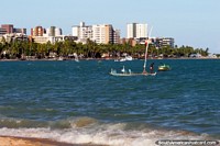 The sea and beach has a backdrop of palm trees and buildings in Maceio. Brazil, South America.