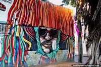 A man has his face buried under his hat and costume, street art in Olinda.