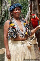 Indigenous woman dressed in traditional clothing holds a macaw, jungle in Manaus. Brazil, South America.