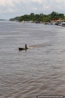 Larger version of Looking upriver in a town in the Amazon, man on a small boat.