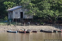 Small wooden river boats moored on the banks of the Amazon river in front of a house.