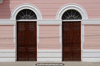Arched doorways with brown wooden doors, white skirting and pink wall in Corumba.