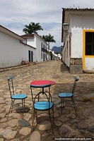 Table and chairs on a long cobblestone street leading down to a church in Paraty.