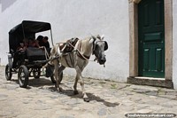 Cavalo branco puxa uma pequena carroa de passageiros pela rua de Paraty.