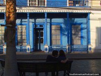 Um par em um benchseat em frente de um edifïcio histórico azul em Iquique. Chile, América do Sul.