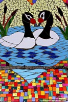 Un par de cisnes en un estanque colorido, asientos diseñados con cuadros de azulejos en Puerto Montt. Chile, Sudamerica.