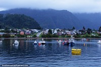 Puerto Cisnes, boats moored in the bay, houses in front of the hills, journey by ferry. Chile, South America.