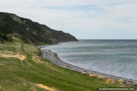 Versión más grande de Playa pedregosa y bancos verdes junto a las aguas alrededor de Tierra del Fuego.