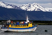 Barco amarelo e azul nas águas com enormes montanhas na distância em Porto Natales. Chile, América do Sul.