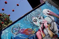 Chica con un pelícano y medusa, mural con bolas de lana roja en una cuerda arriba en Valparaíso.