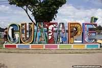 Verso maior do Guatape escrito em grandes letras coloridas em frente  lagoa.