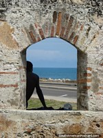 O homem olha para o mar junto de uma janela arcada em uma parede de pedra em Cartagena. Colômbia, América do Sul.