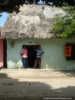 2 hombres charlan en la entrada de una casa del tejado cubierto con paja en Mompos. Colombia, Sudamerica.