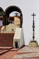 Torre distante a través de un arco, una cruz de acero y escaleras de ladrillo rojo en Guatavita. Colombia, Sudamerica.