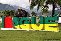 Amo Ibague, gran señal de bienvenida a la ciudad con un tren detrás y colinas distantes. Colombia, Sudamerica.