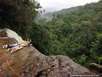 2 people look over the cliff at the End of the World Waterfall while attached to chains in Mocoa. Colombia, South America.