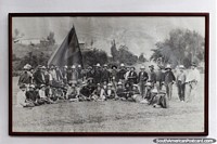 Old black and white photograph of locals of Pamplona, many men in hats with large flag. Colombia, South America.