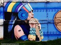 Woman with amazing headgear and wristbands blows wooden pipes, street art in Pasto. Colombia, South America.